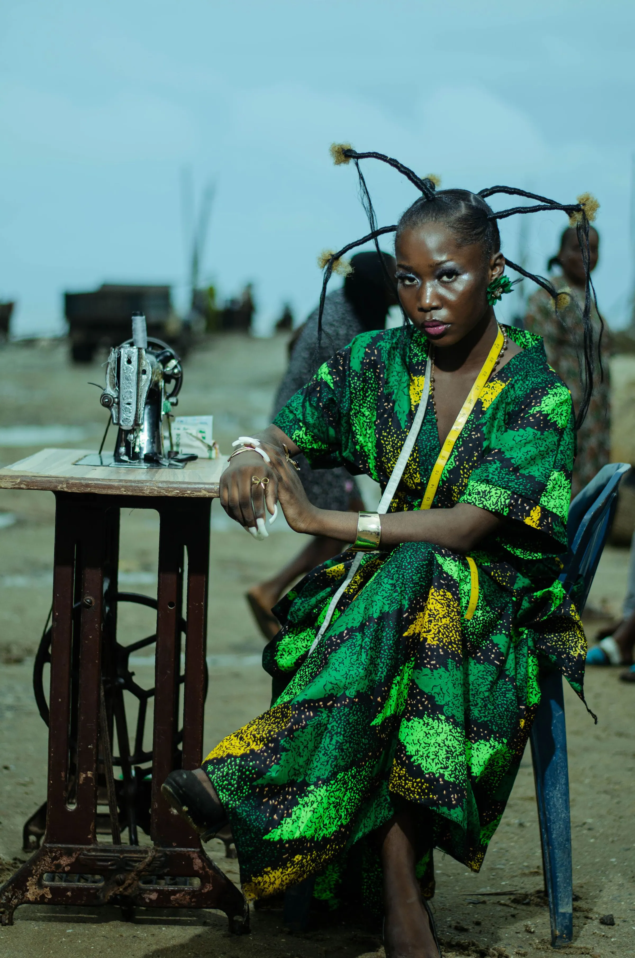 A woman in a green print dress seated beside a sewing machine in Lagos