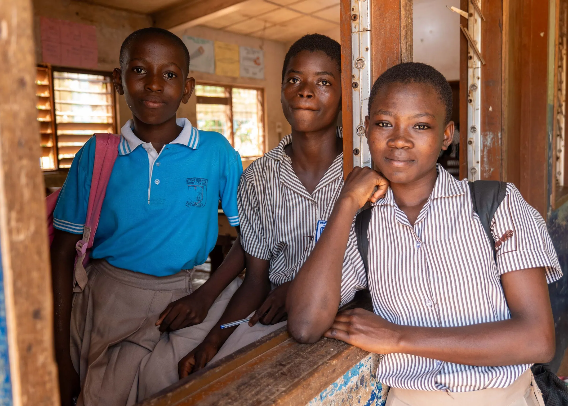Three secondary school students smiling by a classroom window